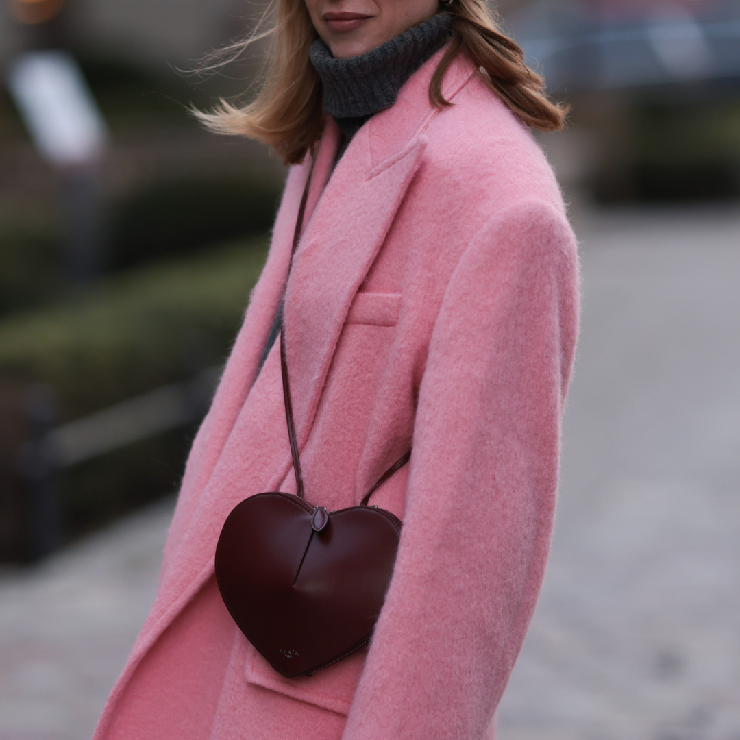 a woman wearing a pink coat and a burgundy heart bag in street style
