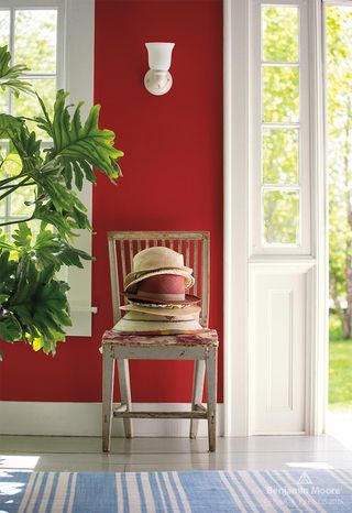 A room painted in a rich red color with a blue striped rug and a vintage distressed chair