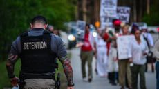 A detention employee walks past anti-ICE protesters in Miami