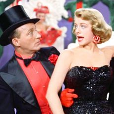 a man and woman in red and black outfits singing in white christmas