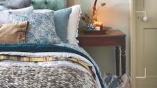 Close up of a cosy bedroom with pale blue upholstered headboard and layers of cushions and blankets to support the question can you sleep with an electric blanket on