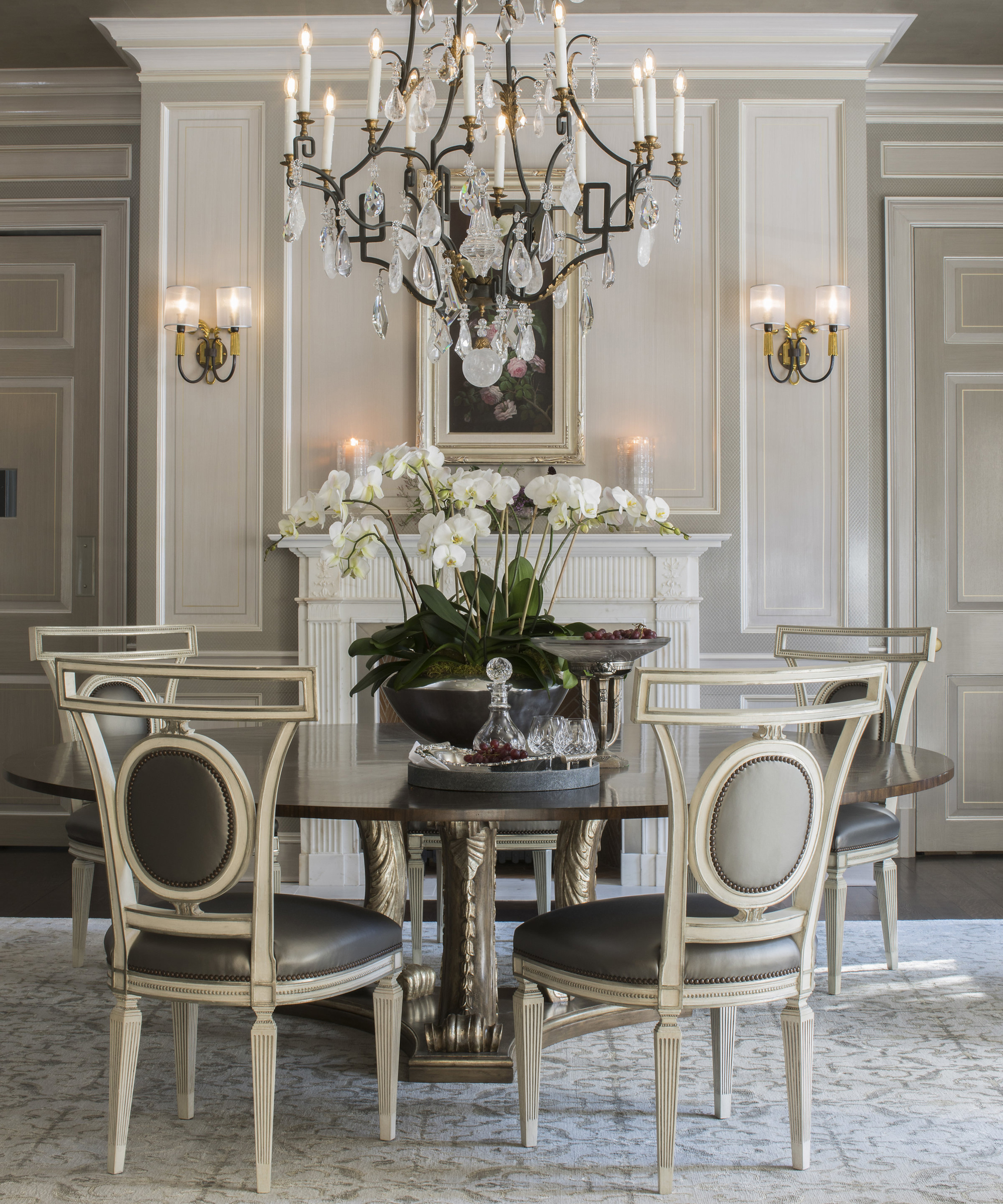 A dining table decor idea with a round table in a grey dining table with chandelier and orchid display in the center