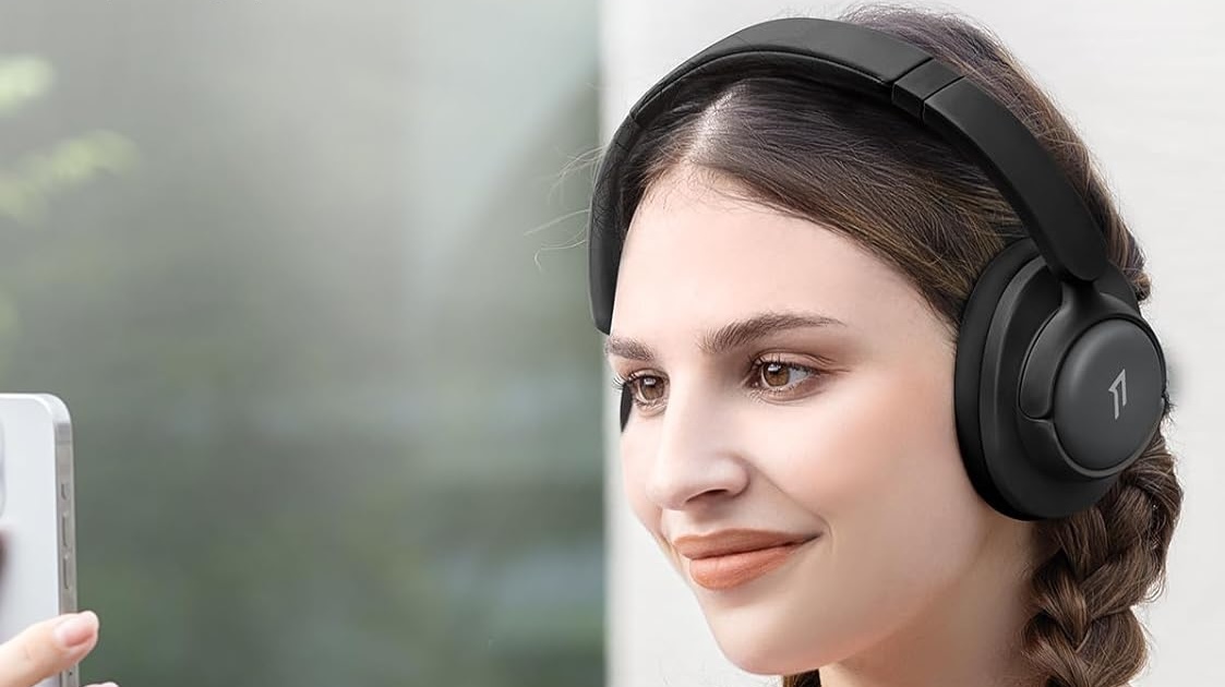 Smiling woman wearing black 1More SonoFlow headphones while looking at phone.