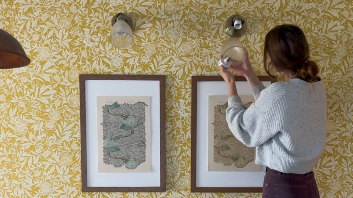 woman hanging lights above pictures on a wall