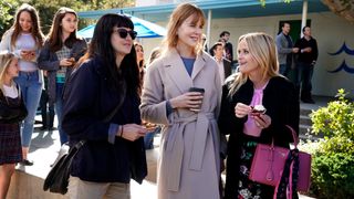 The cast of Big Little Lies wearing coats and drinking coffee in the street