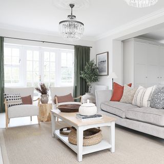 a neutral look living area with a grey/cream sofa, wooden coffee table, green curtains and a pair of statement armchairs