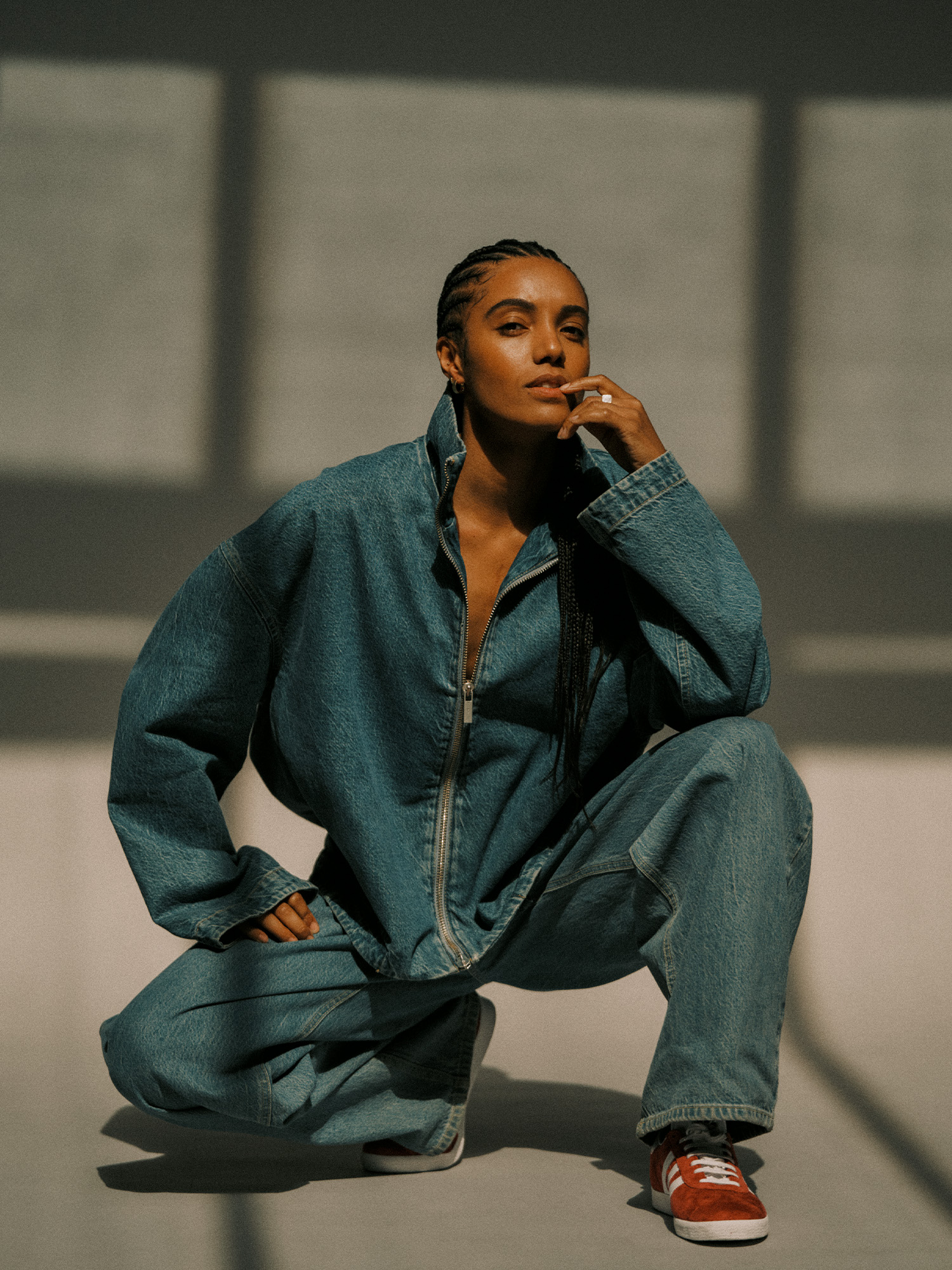 Actor Maisie Richardson-Sellers poses on a gray seamless backdrop wearing an oversize zip-up denim jacket and baggy jeans with red Adidas sneakers.