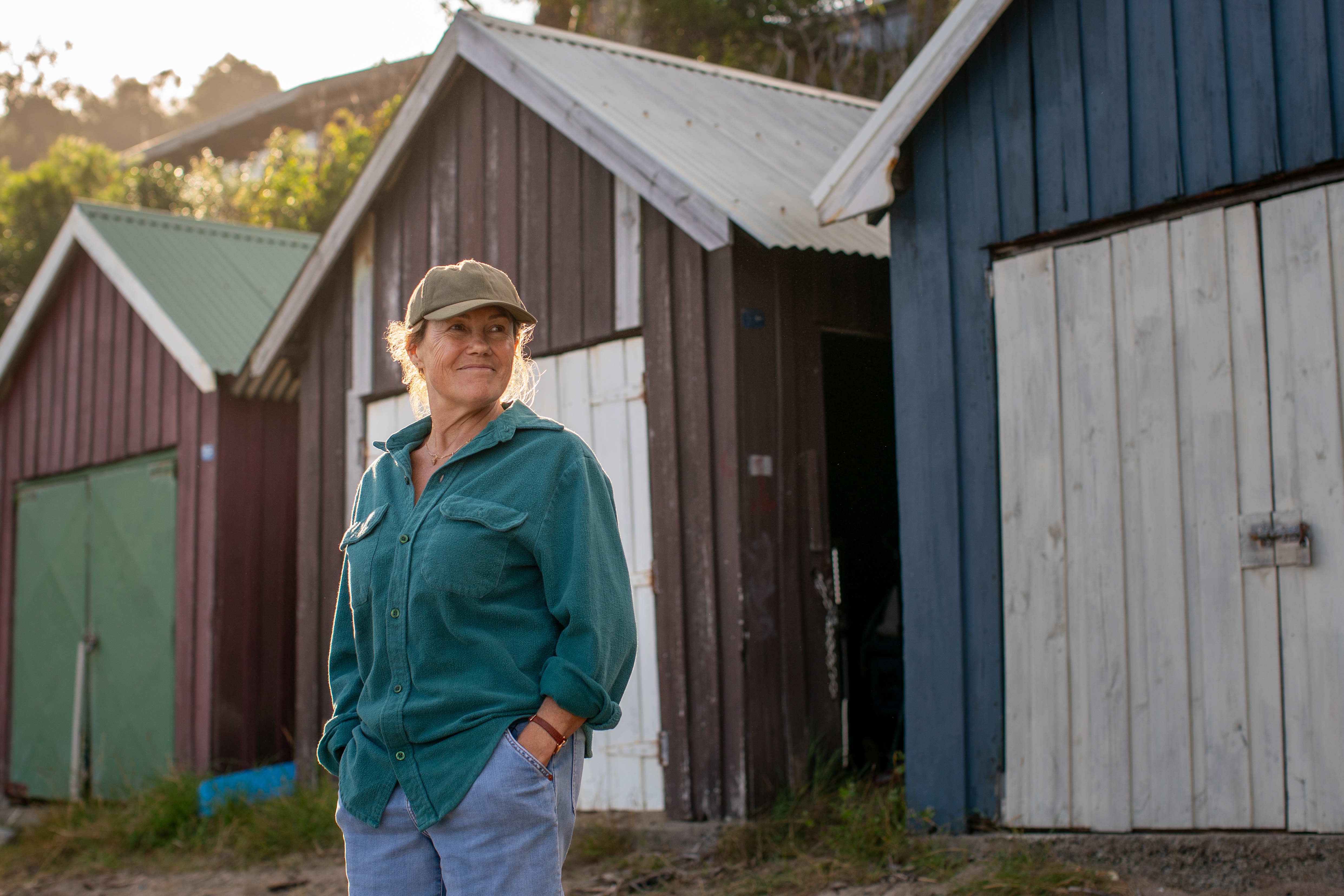 robyn malcolm standing outside of a barn wearing a cap in the netflix mystery the survivors