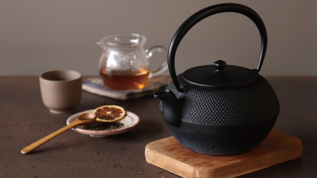 A table with a black teapot, a wooden stand, a small plate, a cup, and a honeypot