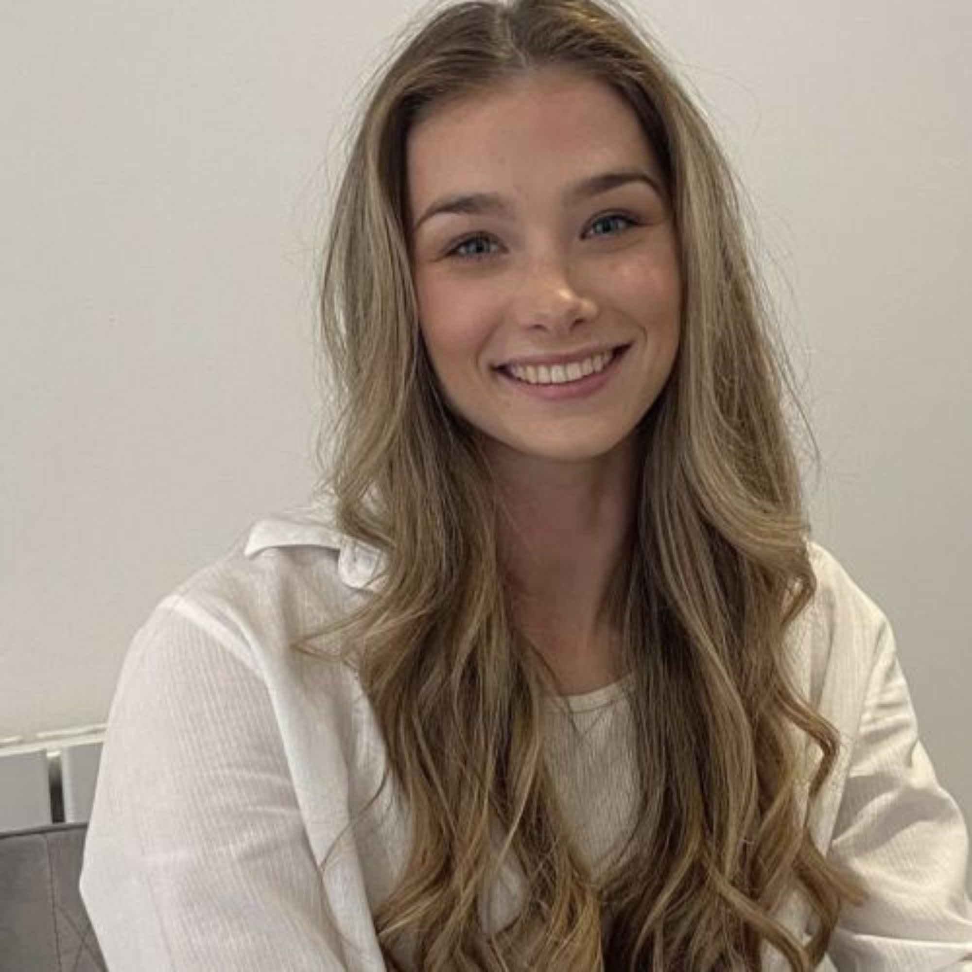 Circular headshot of smiling young woman with long wavy blonde hair, white top, plain background, green border.
