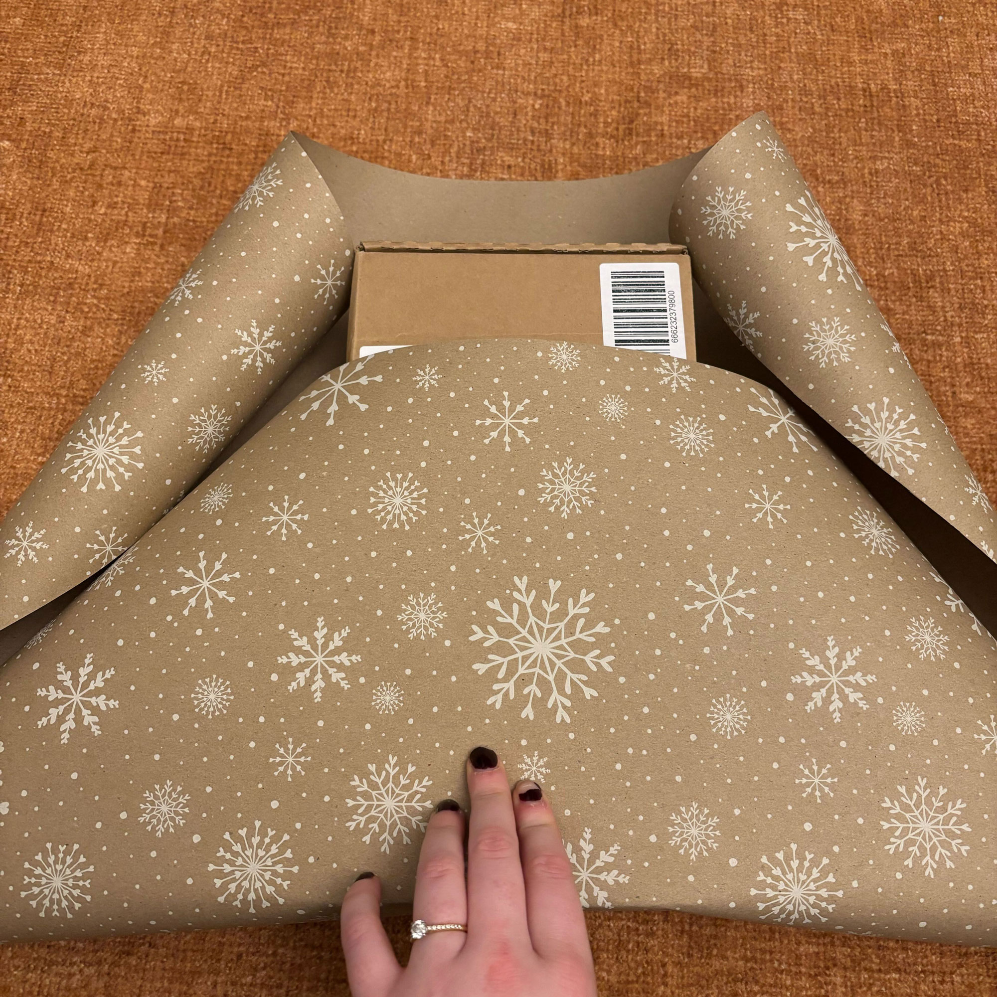 A rectangular box wrapped in brown paper with a white snowflake print on it