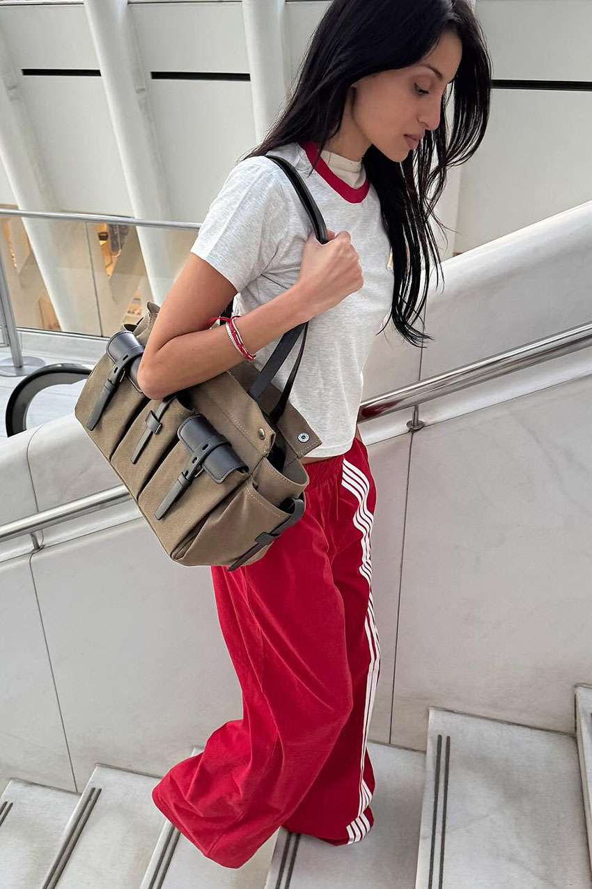 a woman wearing a white and red ringer tee, red baggy track pants, and a Prada shoulder bag