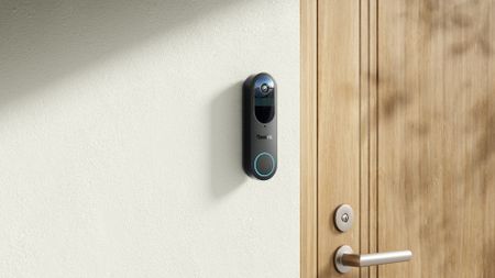Reolink Battery Doorbell installed on a white wall next to wooden door