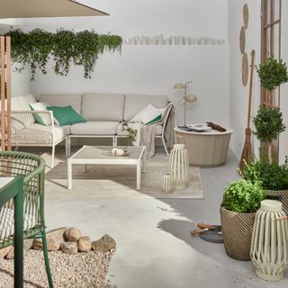 neutral garden with white walls, zoned area with sofa, pebble area with table and chairs, planters, coffee tables, lanterns, greenery