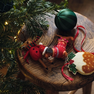 Collection of shaped baubles on a stool. There is a classic green one, Christmas pudding and sausage dog