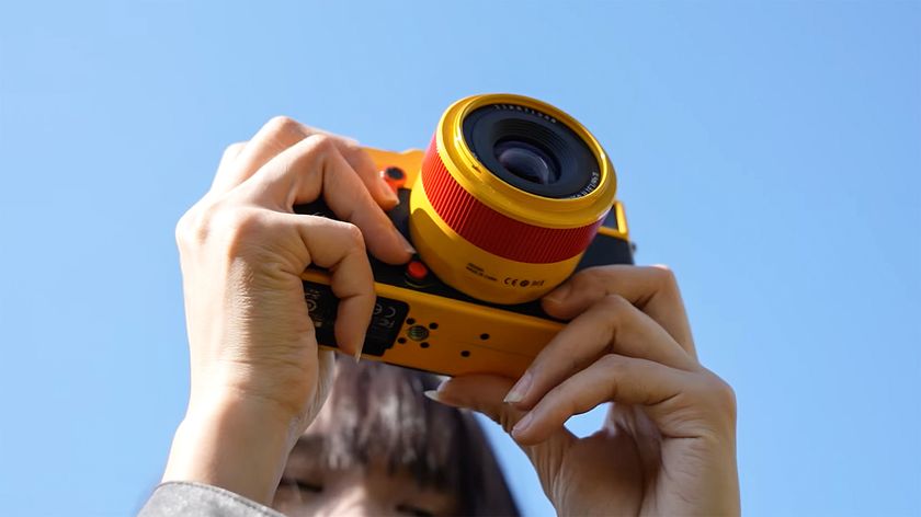 TTArtisan AF 35mm f/1.8 II 'Orange Pop' on yellow and orange camera, held up to blue sky 