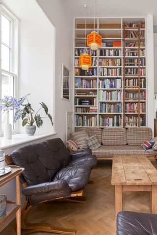 A dark brown sofa and checked sofa in living room in front of bookshelf with lots of books