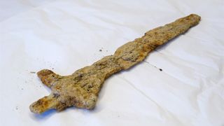 viking sword encrusted in clay on a white surface