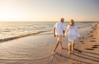 Happy senior couple walking and holding hands on a beach at sunset