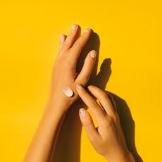 Woman spreading cream on hands with yellow background