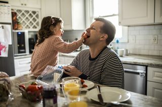young daughter feeding dad a strawberry in the kitchen at home