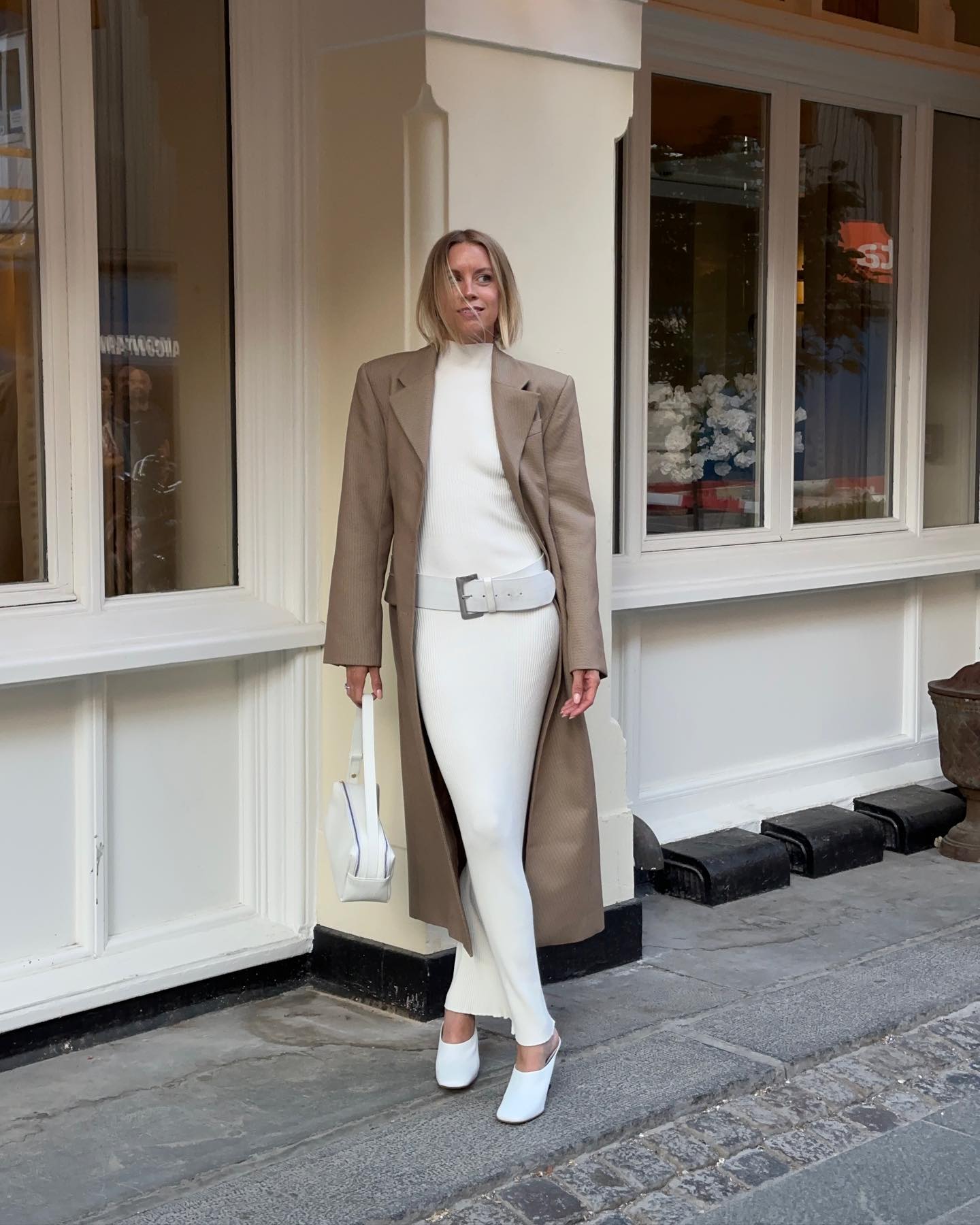 Woman wears white dress, white belt, beige long jacket, white shoes and white bag