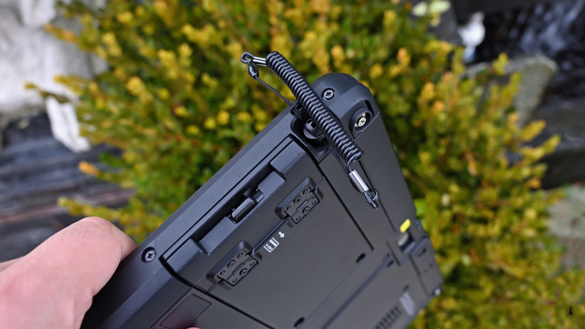 Close-up of the upper rugged chassis of a Panasonic TOUGHBOOK 34 showing an attached coiled stylus tether.