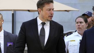 Elon Musk talking to another person with guard in the background