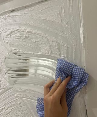 Wiping shaving foam off a mirror with a white wooden border using a blue and white J cloth