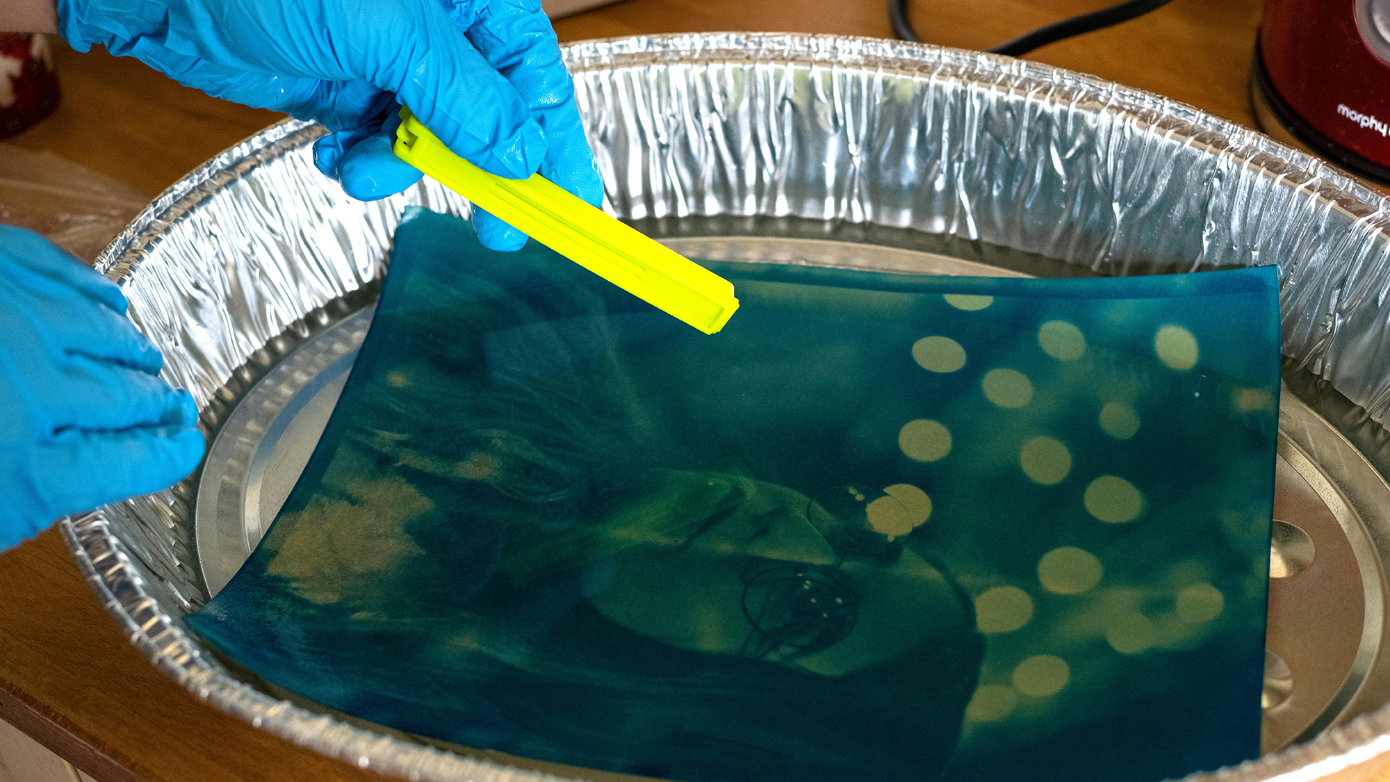 Gloved hands placing exposed print into acidic solution to develop print