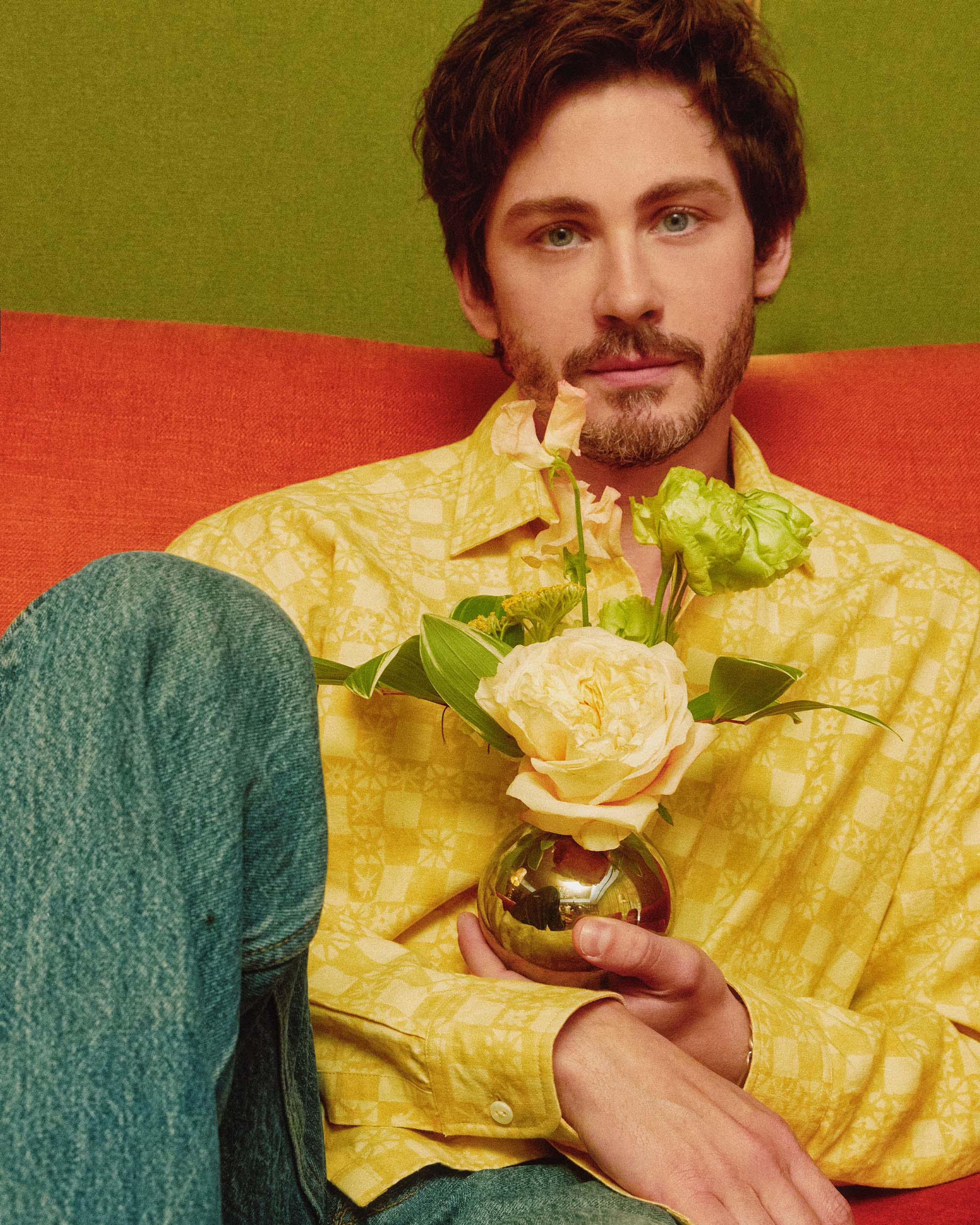 Logan Lerman wears a yellow shirt and holds a yellow rose in a vase