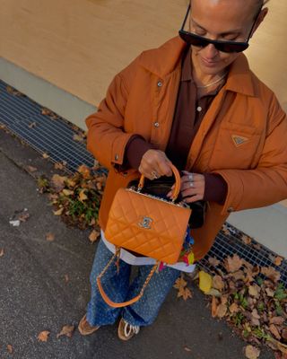 woman wearing an orange prada coat with an orange chanel bag with charms and jeans