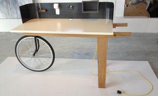 A wooden table, with a bicycle wheel replacing a table leg.