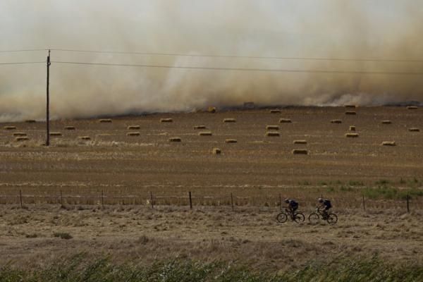 A fire rages in a field as riders battle the head wind during stage 4