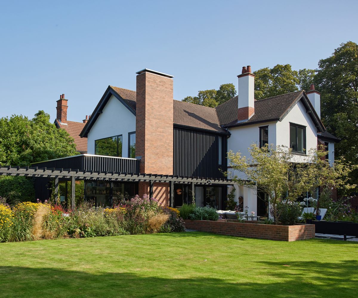 large white rendered house with black cladding on one side matching finish of new rear extension and terrace