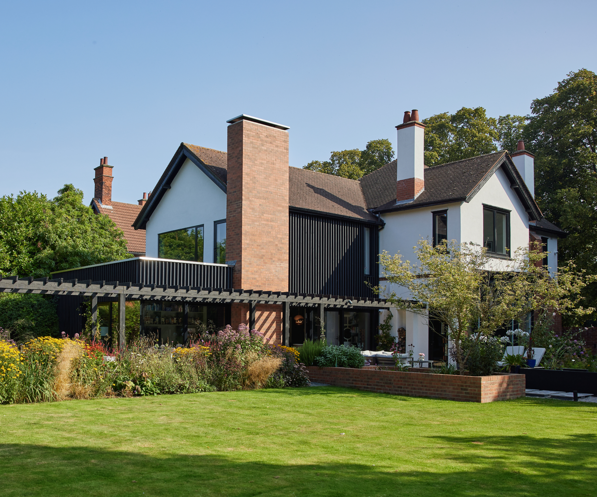 large white rendered house with black cladding on one side matching finish of new rear extension and terrace