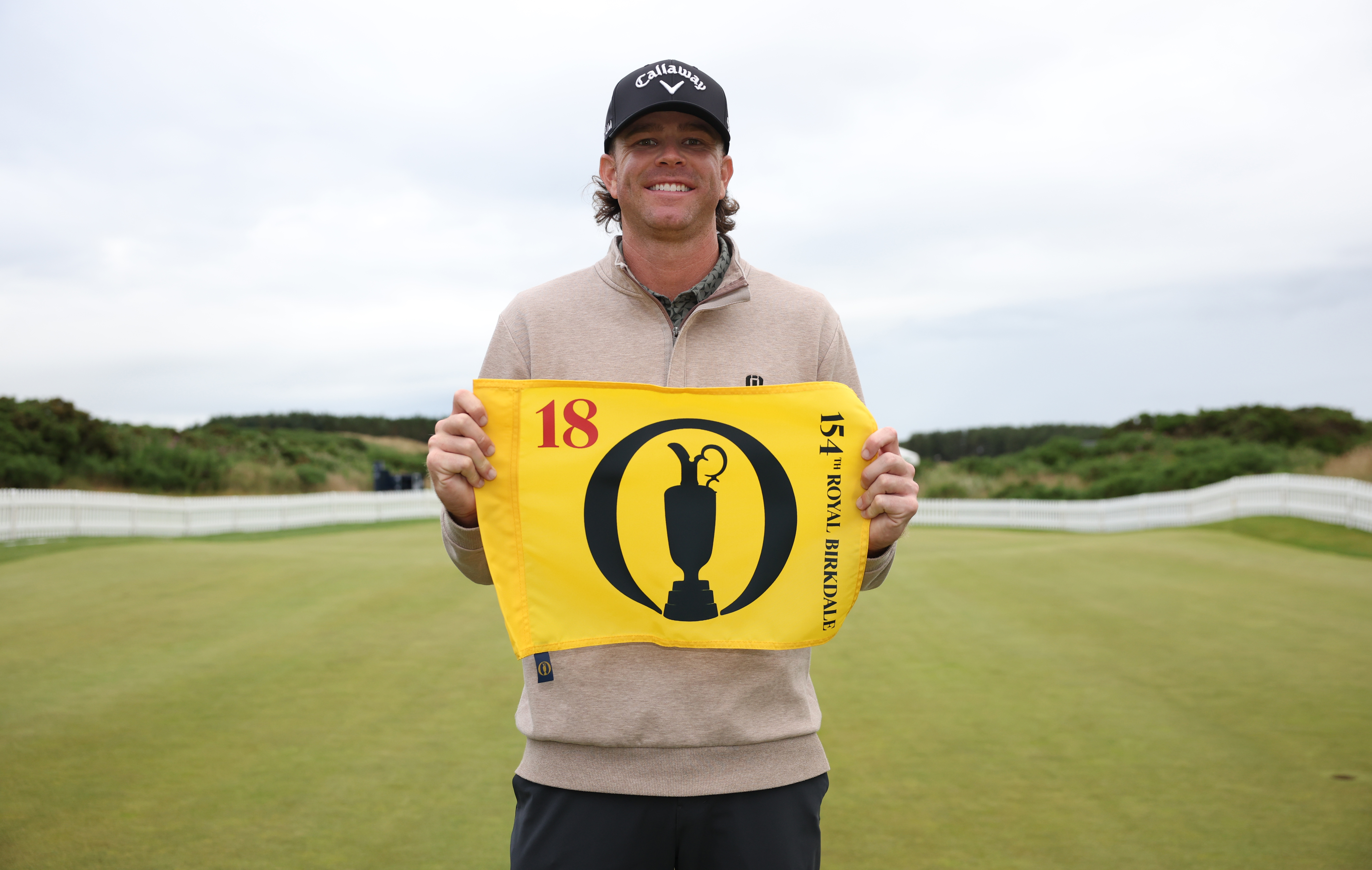 Marcus Plunkett poses with an Open flag after making it through Final Qualifying at Dundonald Links in 2026