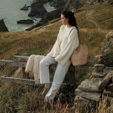 Jessica wears an ivory sweater, straw bag, white jeans, and tan clogs.