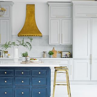 white kitchen with blue island and brass cooker hood