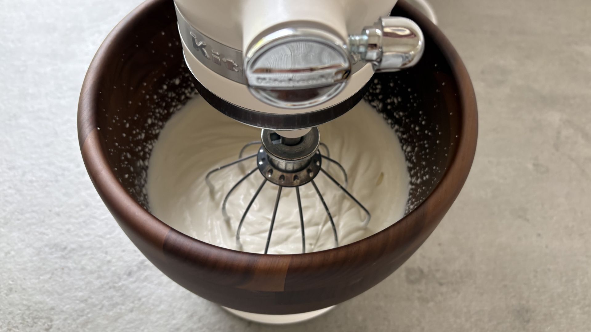 KitchenAid Artisan Stand Mixer with Wooden Bowl on the counter whipping cream