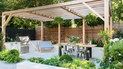 a wicker hanging chair on a raised patio with a wicker table beside it and plenty of planters