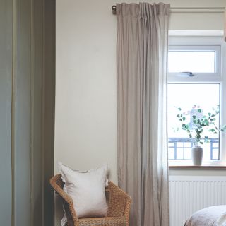 A bedroom window with curtains and a rattan chair