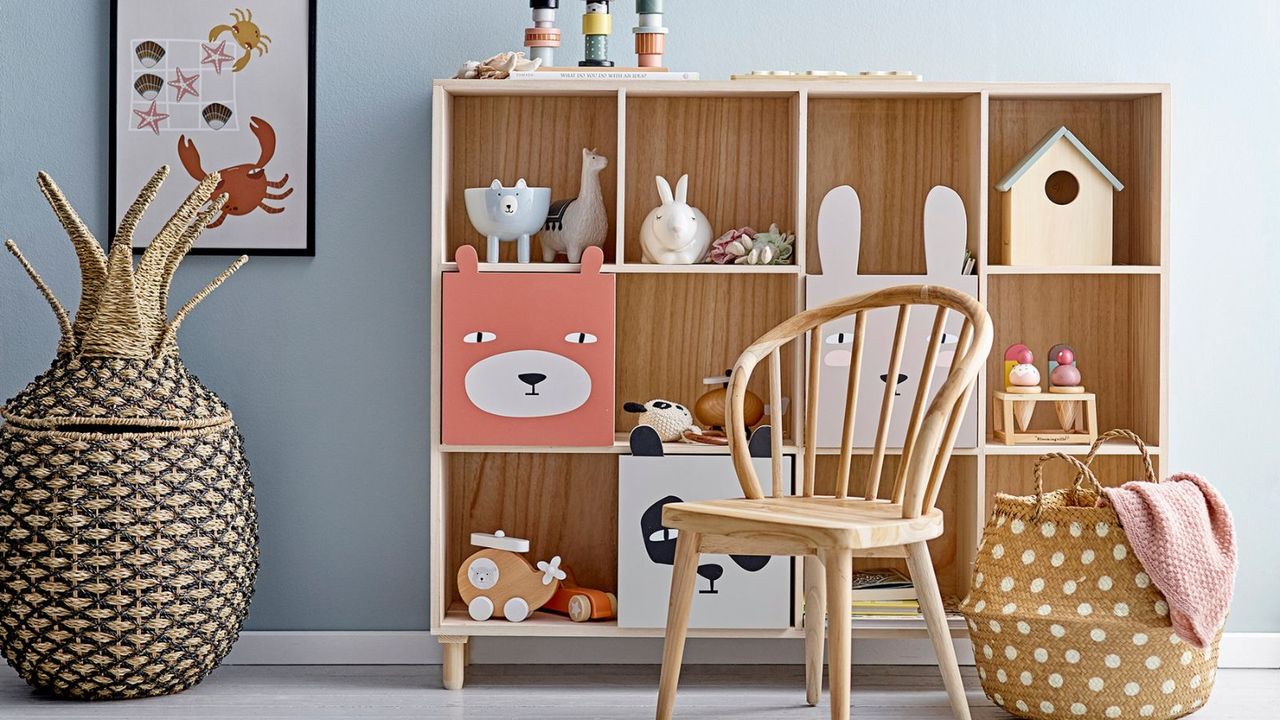 A blue children&#039;s bedroom with a wooden square cubby bookcase filled with toys. A wooden chair in front of it, and a basket for blankets 