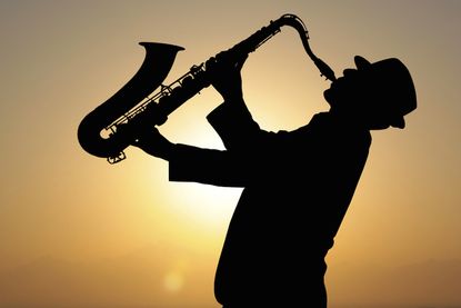 A man plays a saxophone in front of a sunset
