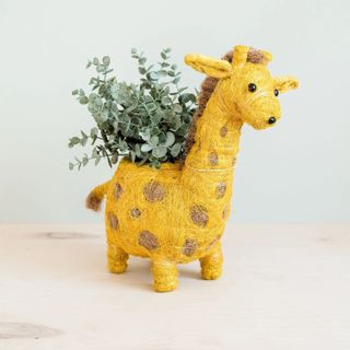 A Likha planter shaped like a yellow giraffe with an artificial green plant inside