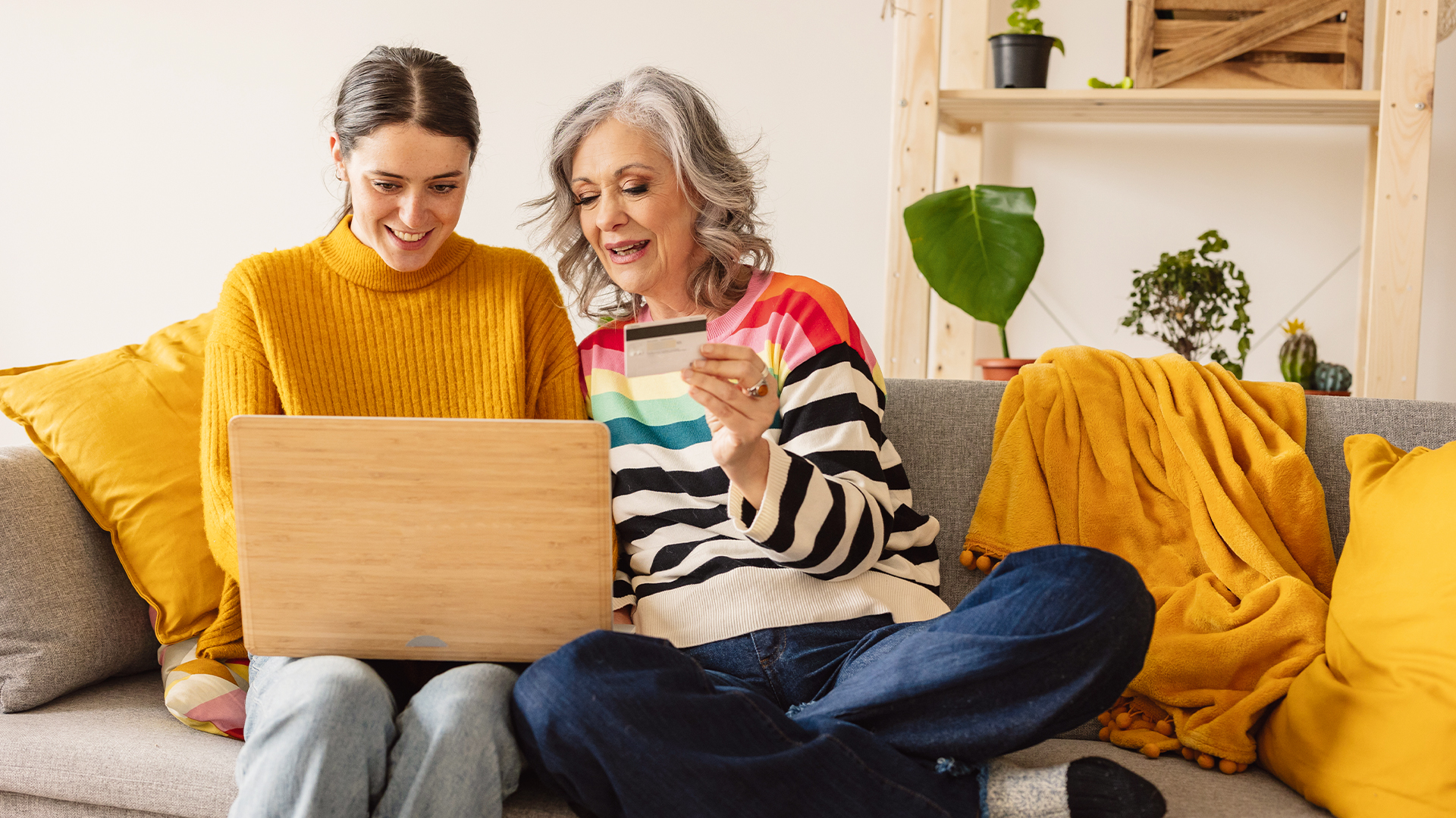 Two women sit on the sofa, both looking at a laptop with smiles on their faces