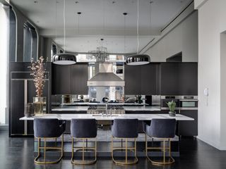 A mirrored kitchen with hanging light fixtures, island, stools and dried plant
