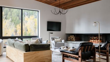 modern living room with timber ceiling, tv on wall, long low modern fireplace, with timber sofa, and vintage armchairs