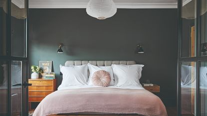 A bedroom with walls painted in soft peach and with a pillow headboard above the bed