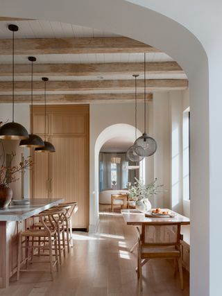 A view through an arched doorway to a dining room with warm woods and hanging pendants